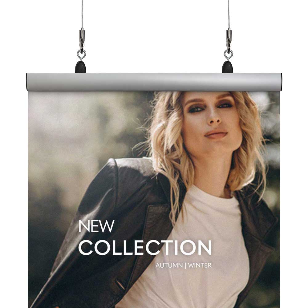 Image shows a poster clamp sign being hung via two cables and safe hooks from the top left and right corners. Sign shows a woman wearing a coat and reads 'New collection autumn winter'