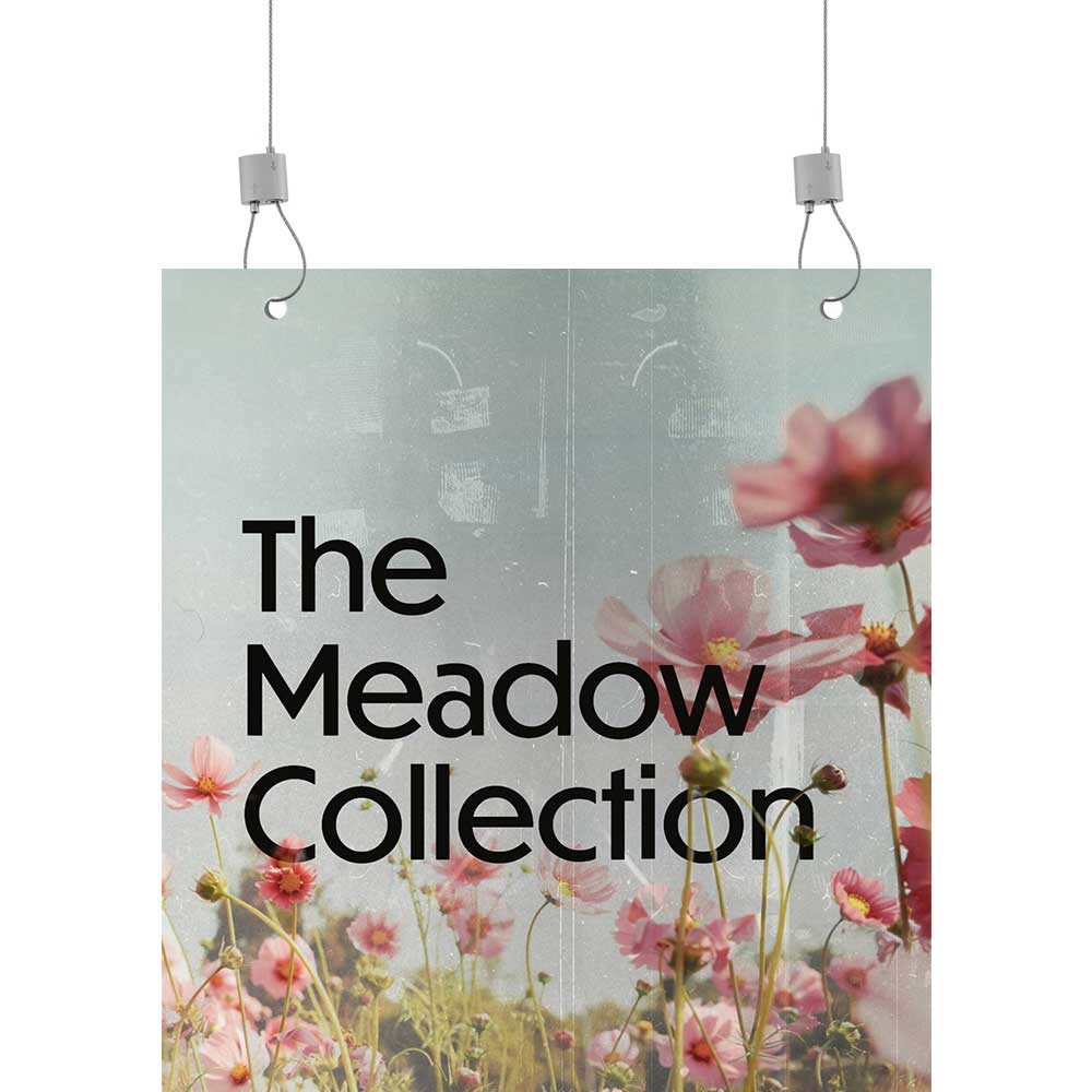 Image shows a sign being hung via two cables and urban trapeze's from the top left and right corners. The sign shows pink flowers and reads 'the meadow collection'.