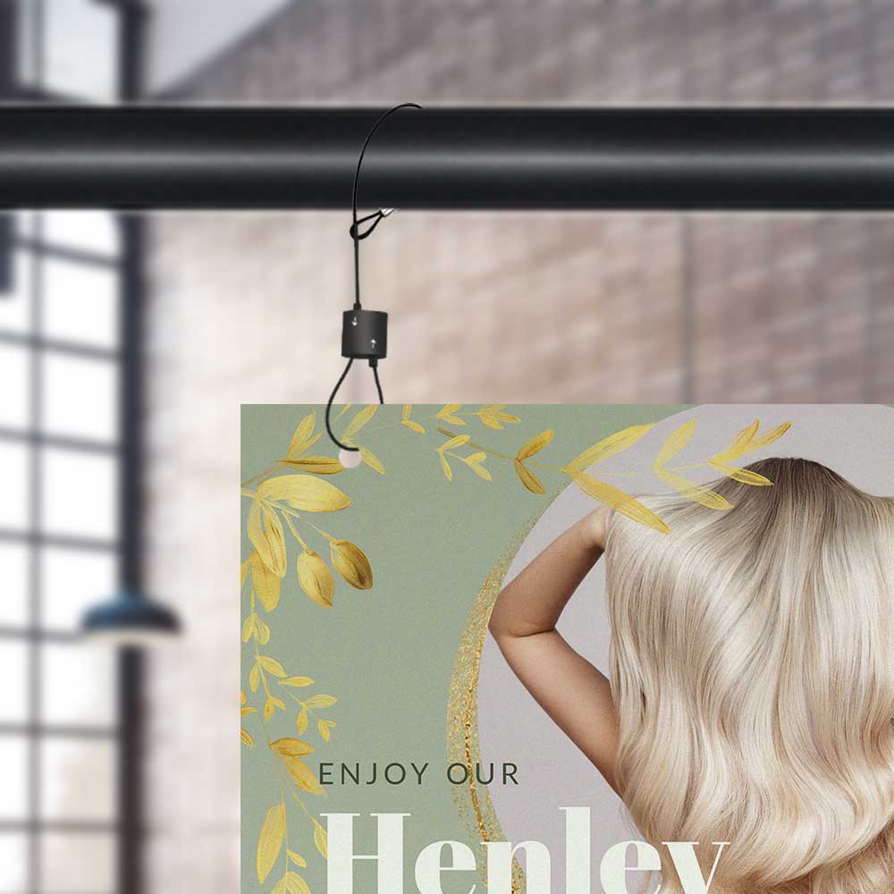 Image shows a the top left corner of a sign being hung via a black cable and urban trapeze from a pole. The sign shows a woman's blonde hair and reads 'enjoy our henley' in a shop.